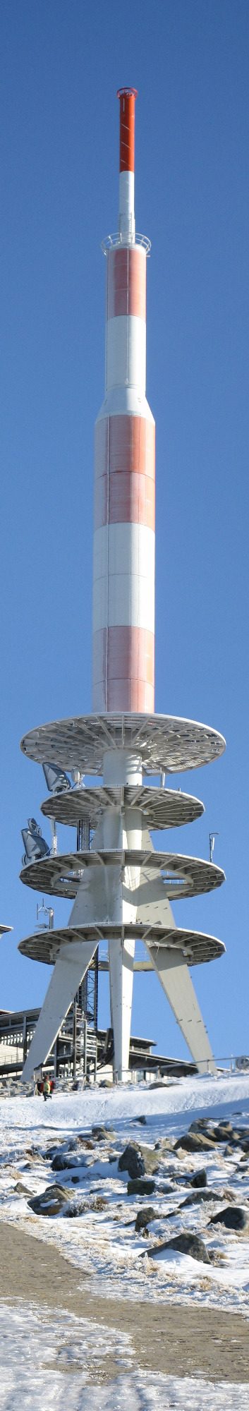 Fernmeldeturm mit rot-weißer Markierung, umgeben von Schnee und klarem Himmel.