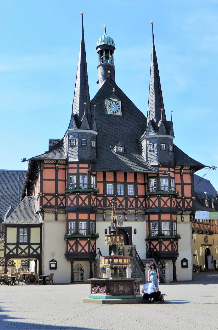 Historisches Rathaus mit spitzen Türmen und Brunnen im Vordergrund, blauer Himmel.